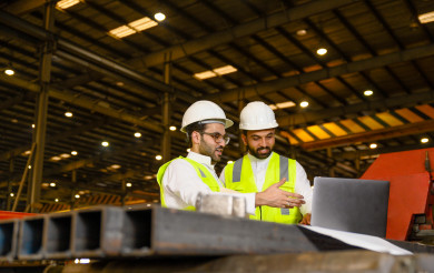 مشرفان سعوديين داخل مصنع الحديد ، يحمل احدهم ملف الملاحظات ، يقومون بتتبع العمل من خلال الكمبيوتر المحمول و مخطط المصنع 