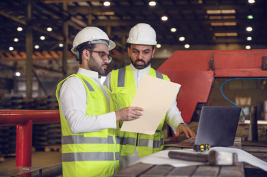 مشرفان سعوديين داخل مصنع الحديد ، يحمل احدهم ملف الملاحظات ، يقومون بتتبع العمل من خلال الكمبيوتر المحمول و مخطط المصنع 