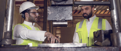 مهندسان صناعيان سعوديين شركاء في مصنع الحديد، يقفان بجانب آلة تصنيع الحديد ، يتناقشان في جودة انتاج المصنع ، الاشراف على انتاجية الحديد و الألمنيوم في المصنع