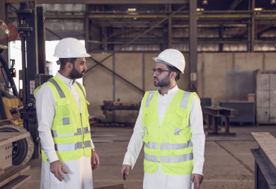 مهندسان صناعيان سعوديين في اجتماع داخل مصنع الحديد ، لتطوير آلية انتاجها ، ارتداء خوذة  و سترة الحماية الخاصة بالعمل