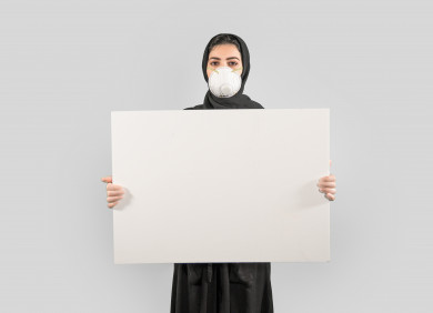 بورتريه لشابة سعودية تضع الكمامة ،  تحمل بيدها لوح ابيض فارغ ، اتباع اجراءات السلامة بوضع الكمامة بشكل صحيح ، تجنب انتشار العدوى ، خلفية بيضاء