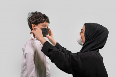 بورتريه لشابة سعودية تضع الكمامة  و تعلم ابنها وضع الكمامة ، اتباع اجراءات السلامة بوضع الكمامة بشكل صحيح ، تجنب انتشار العدوى ، خلفية بيضاء