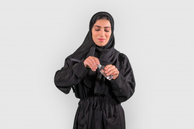 بورتريه لشابة سعودية تقوم بتعقيم يديها ، اتباع اجراءات السلامة باستخدام معقم اليدين ، تجنب انتشار العدوى ، خلفية بيضاء