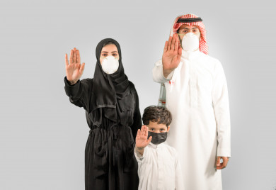 بورتريه عائلة سعودية من أب و ام و الابن و ترتدي الكمامة ، يرفعون ايدهم لتجنب المصافحة واقتراب الاخرين منهم ، تجنب انتشار العدوى ، الحفاظ على المسافات ، خلفية بيضاء