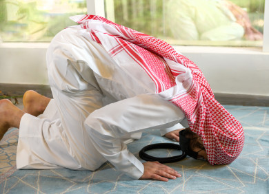 رجل سعودي خليجي ملتزم باتباع اجراءات السلامة بوضع الكمامة بشكل صحيح اثناء الصلاه في المسجد  ، تجنب انتشار العدوى ، خلفية بيضاء