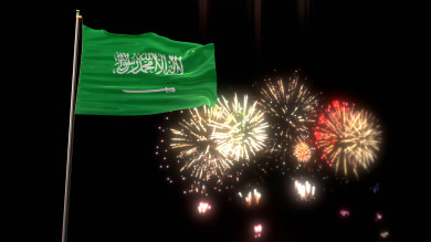 علم السعودية يرفرف في السماء مع العاب نارية في الخلفية ، احتفالات اليوم الوطني السعودي ،موسم الرياض