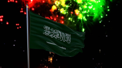 علم السعودية يرفرف في السماء مع العاب نارية في الخلفية ، احتفالات اليوم الوطني السعودي ،موسم الرياض