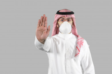 بورتريه لشاب سعودي يرتدي الكمامة ، يرفع يده ليتجنب المصافحة واقتراب الاخرين منه ، تجنب انتشار العدوى ، الحفاظ على المسافات ، خلفية بيضاء