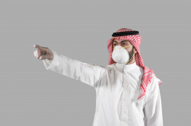 بورتريه لشاب سعودي يرتدي الكمامة و القفازات ، يرفع يده و يؤشر باصبعة على مكان ، تجنب انتشار العدوى ، الحفاظ على المسافات ، خلفية بيضاء