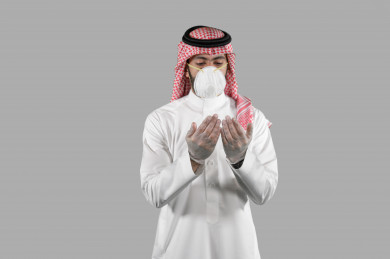 بورتريه لشاب سعودي يرتدي الكمامة و القفازات ، يرفع يده لاعلى و يدعو الله ، تجنب انتشار العدوى ، الحفاظ على المسافات ، خلفية بيضاء