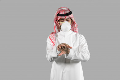 بورتريه لشاب سعودي يقوم بتعقيم يديه ، اتباع اجراءات السلامة باستخدام معقم اليدين ، تجنب انتشار العدوى ، خلفية بيضاء