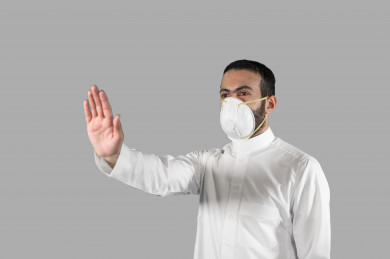 بورتريه لشاب سعودي يرتدي الكمامة ، يرفع يده ليتجنب المصافحة واقتراب الاخرين منه ، تجنب انتشار العدوى ، الحفاظ على المسافات ، خلفية بيضاء