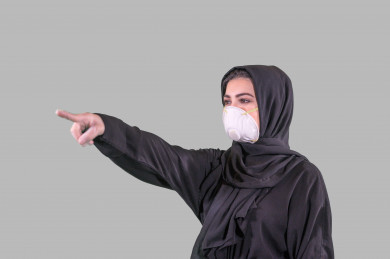بورتريه لفتاه سعودية ترتدي الكمامة و القفازات ، ترفع يدها و تؤشر باصبعها على مكان ، تجنب انتشار العدوى ، الحفاظ على المسافات ، خلفية بيضاء