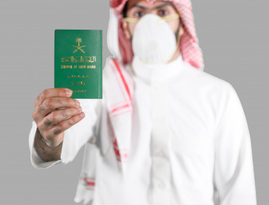رجل سعودي خليجي مسافر يحمل بيده جواز سفر سعودي  ، ملتزم باتباع اجراءات السلامة بوضع الكمامة بشكل صحيح اثناء السفر  ، تجنب انتشار العدوى ، خلفية بيضاء