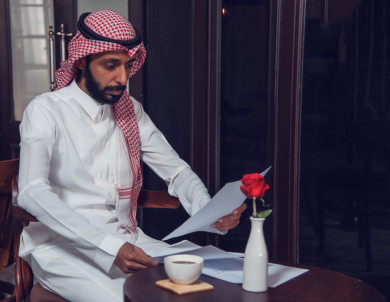 رجل أعمال عربي سعودي سعيد ،يعمل في المقهى و يحمل بيده أوراق رسمية ، بجانبه  فنجان القهوة ،  متجر القهوه