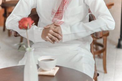 رجل عربي سعودي سعيد  يجلس في المقهى  ، ومعه كوب القهوة ، طلب القهوه في متجر القهوه