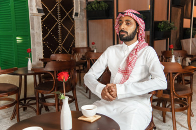 رجل عربي سعودي سعيد  يجلس في المقهى  ، ومعه كوب القهوة ، طلب القهوه في متجر القهوه