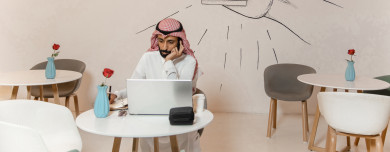 رجل أعمال عربي سعودي سعيد ، يعمل على الكمبيوتر المحمول ، ويستقبل مكالمة على هاتفه المحمول ،  متجر القهوه