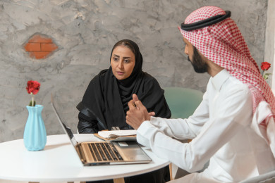 رجل أعمال و سيدة أعمال عربيان  سعوديان في اجتماع عمل داخل المقهى ، يعملان على الكمبيوتر المحمول ،  متجر القهوه