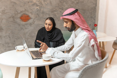 رجل أعمال و سيدة أعمال عربيان  سعوديان في اجتماع عمل داخل المقهى ، يعملان على الكمبيوتر المحمول ،  متجر القهوه