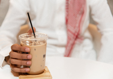 رجل عربي سعودي سعيد  يجلس في المقهى و يحمل ميلك شيك  ، طلب القهوه الباردة  في متجر القهوه