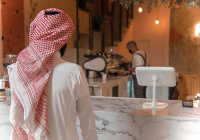 رجل عربي سعودي ينتظر طلبه عند الاستقبال ، طلب القهوه في متجر القهوه