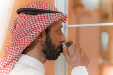 رجل عربي سعودي يشرب قهوته بالقرب من نافذة المقهى ، طلب القهوه في متجر القهوه